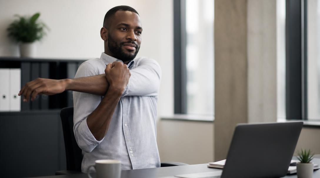 A Black professional man taking a short mobility break at his desk